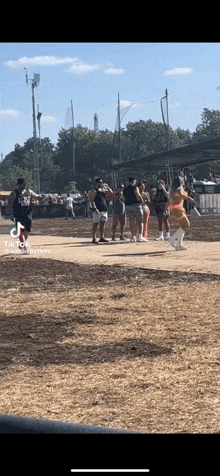 a group of people are standing on a dirt field watching a cheerleader .