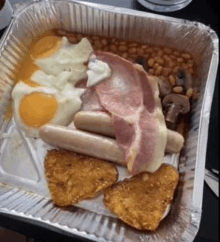 a foil container filled with eggs , bacon , sausages , beans and hash browns