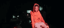 a young man in an orange hoodie is sitting in a dark room .