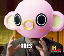 a man in a suit and tie is wearing a pink monkey mask with the words `` toes '' written on it .