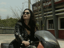 a woman wearing sunglasses is riding a motorcycle in front of a building with the word mateo on it