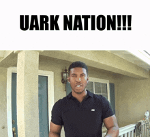 a man in a black shirt stands in front of a house with the words uark nation written above him