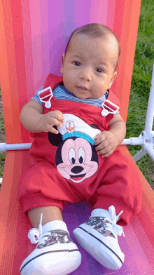 a baby wearing a red mickey mouse outfit sits on a chair