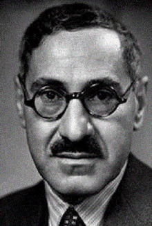 a man wearing glasses and a suit and tie looks at the camera