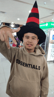 a man wearing a hoodie that says essentials is wearing a witch hat