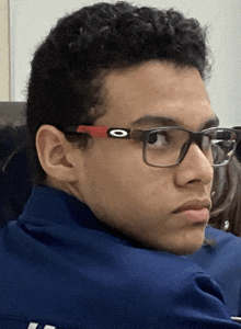 a young man wearing glasses and a blue shirt with the letter o on it