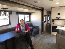 a woman in a pink jacket is sitting at a table in a camper