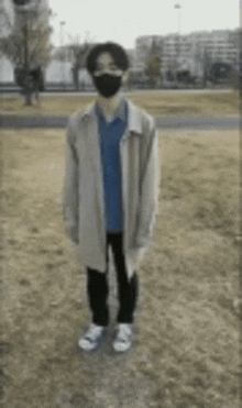 a young man wearing a mask and a trench coat is standing in a field .