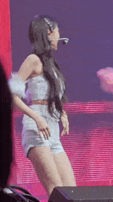 a woman in a crop top and shorts is dancing on a stage with a microphone .