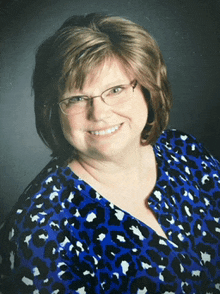 a woman wearing glasses and a blue shirt is smiling