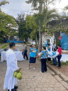 a priest is holding a bunch of fruit while standing next to a group of people on a sidewalk .