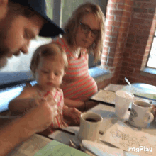 a pregnant woman sits at a table with a little girl and a man while a cup of coffee sits on the table