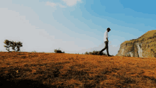 a man in a white shirt is walking on a hillside