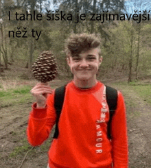 a young man in a red sweatshirt is holding a pine cone in his hand .