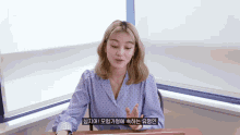 a woman in a polka dot shirt is sitting at a desk in front of a window and talking in a foreign language