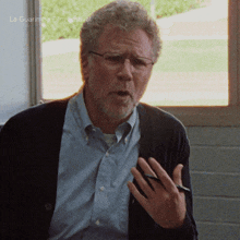 a man wearing glasses and a cardigan is talking in front of a window with la guarimba film festival written on the bottom