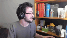 a man wearing headphones and glasses stands in front of a shelf full of books one of which is titled harfap