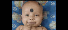 a baby with a black spot on his forehead is laying on a blue blanket