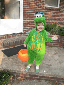 a little boy dressed in a frog costume is holding an orange bucket