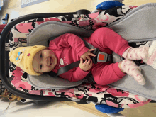 a baby wearing a pink outfit and a yellow hat is sitting in a car seat and smiling