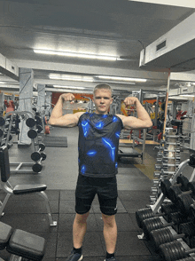 a man flexes his muscles in a gym wearing a blue shirt