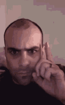 a man with a ring on his finger is making a funny face while holding his finger to his ear .