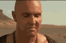 a bald man is standing in the desert with his eyes closed and his mouth open .