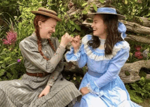 two girls in blue dresses and hats are sitting next to each other and laughing