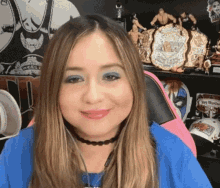 a woman wearing blue eye shadow and a choker is smiling in front of a shelf with wrestling trophies .