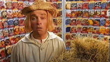 a man wearing a straw hat is holding a bale of hay in front of a display of seeds .