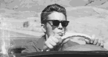 a man wearing sunglasses is driving a car and smoking a cigarette .