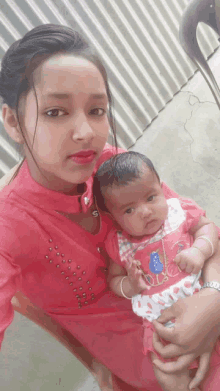 a woman in a pink dress is holding a baby wearing a shirt that says duck