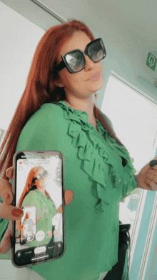 a woman wearing sunglasses and a green shirt holds a cell phone