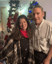 a man and a woman are posing in front of a christmas tree