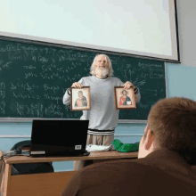 a man with a beard holds up two framed pictures in front of a chalkboard that says ' a ' on it