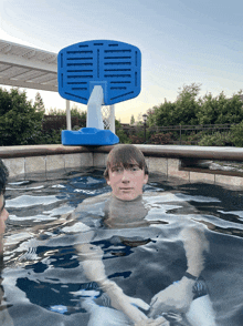 a boy is swimming in a pool with a blue basketball hoop in the background