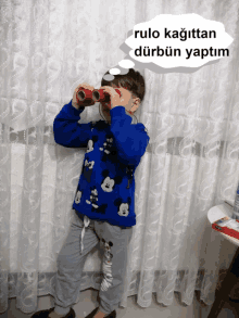 a young boy in a blue mickey mouse sweater looks through binoculars