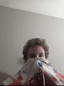 a man with curly hair is covering his face with a sweatshirt with a snake on it