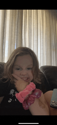 a little girl sitting on a couch with a pink scrunchie on her arm