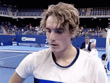 a young man is standing on a tennis court wearing a white shirt with the word adidas on it .