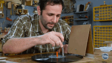 a man in a plaid shirt is working on a piece of wood with the word mundo on the bottom of the image