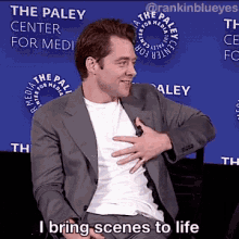 a man in a suit and white shirt is sitting in front of a sign that says the paley center for media