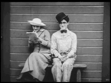 a black and white photo of a man and woman sitting on a bench with mg written on the bottom