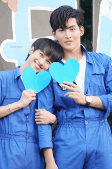 two men in blue jumpsuits hold blue hearts in front of a sign that says " i team sandai "