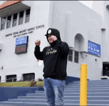 a man wearing a black hoodie stands in front of a white building that says griffith steam magnet middle school