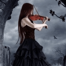 a woman in a black dress is playing a violin in a forest .