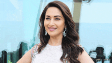 a woman wearing earrings and a white dress smiles for the camera