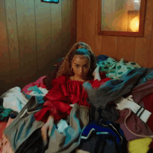 a woman is laying on a bed with a bunch of clothes