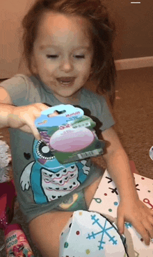 a little girl is sitting on the floor holding a package of soap .