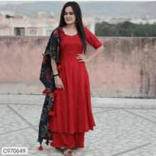 a woman is wearing a red dress with a black dupatta and standing on a rooftop .